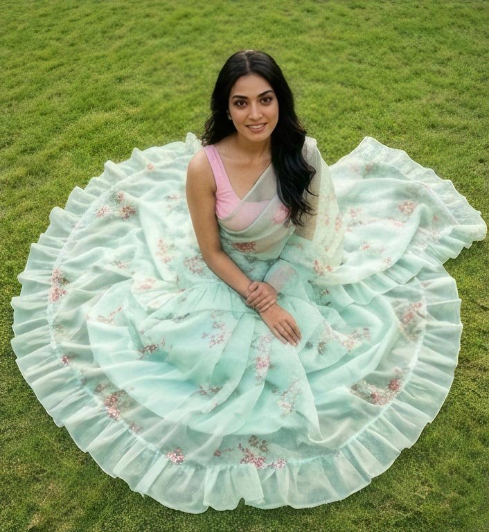 High angle view of a woman sitting on green grass spreading out the flare of her pastel mint green saree.