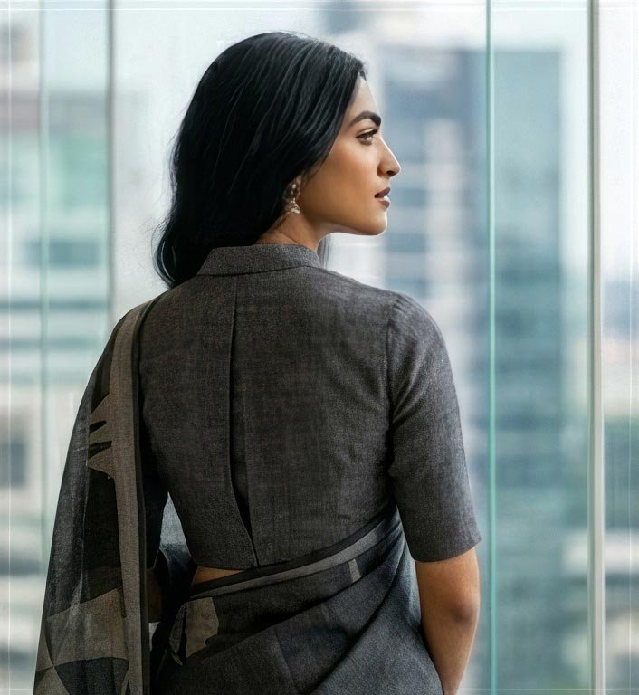 Over-the-shoulder looking back pose of a woman in a grey cotton saree with a high-rise city view.