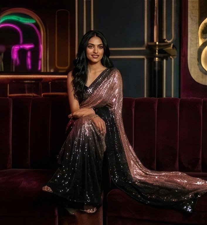 A woman lounging on a dark velvet couch with her glittery sequin saree pallu elegantly draped across.